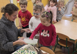 Dzieci po kolei odciskają swoje paluszki na przedszkolnym drzewie.