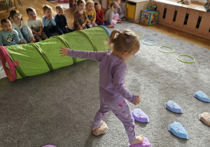 Dzieci ćwiczą swoją równowagę. Po kolei przechodzą po kamieniach.