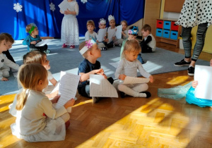 Dzieci siedzą w siadzie skrzyżnym , w ręku trzymają kartki papieru- czekają na wyjaśnienie zadania.