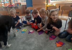 Dzieci siedzą na dywanie w towarzystwie Lili.