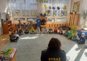 Grupa dzieci uczestniczy w pogadance ze Strażnikiem Miejskim.