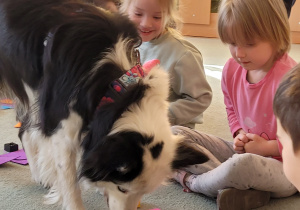 Dziewczynki patrzą na psa, który zjada przysmak.