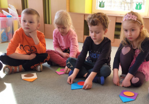 Dzieci siedzą na dywanie i ukłądają budę z figur geometrycznych.