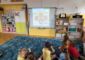 Dzieci oglądają prezentację multimedialną dotyczącą pszczół.