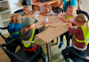 Dzieci siedzą przy stolikach, kolorują kredkami sklejkowe sylwety dinozaurów.