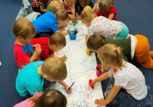 Dzieci kolorują wspólnie obrazek ułożony na dywanie.