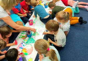 Dzieci zgodnie współpracują, kolorując dużą kolorowankę.