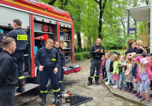 Dzieci słuchają do czego służą przedmioty znajdujące się w wozie strażackim.