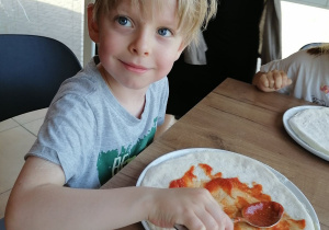 Chłopiec smaruję pizze sosem.