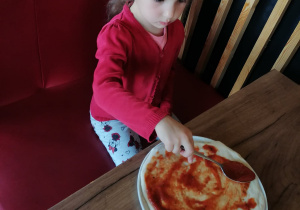 Dziewczynka posmarowała pizze sosem.