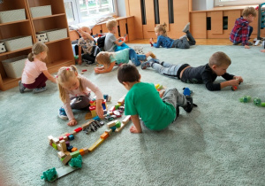 Dzieci bawią się na dywanie- tworzą budowle z drewnianych klocków, bawią się klockami lego.