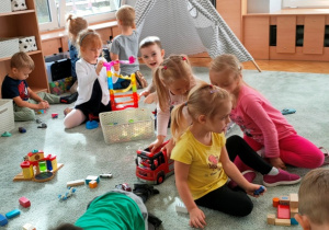 Dzieci bawią się na dywanie różnymi zabawkami.