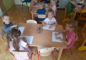 Dzieci siedzą przy stoliku i wykonują kartę pracy.