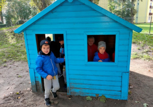 Dzieci kryją się w niebieskim drewnianym domku.