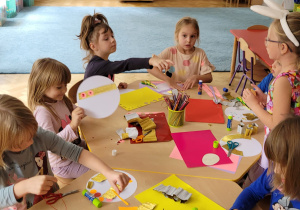 Dzieci przy stolikach wycinają i naklejają kolorowe ozdoby.