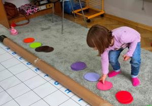 Dziewczynka podnosi z dywanu krążki w wybranym przez siebie kolorze.