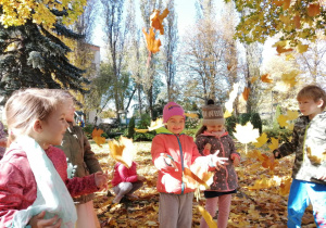 Dzieci podrzucają liście do góry.