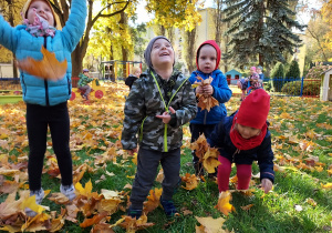 Dzieci podrzucają kolorowe liście do góry.