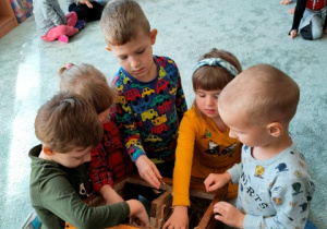 Grupka dzieci ogląda jak wygląda w środku domek dla jeża. Wkłada do środka słomę, aby jeżykowi w zimę było ciepło.