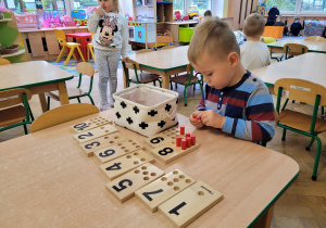 Chłopiec układa drewniane tabliczki z cyframi.