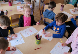 Dzieci przy stolikach rozwiązują samodzielnie dyktando graficzne.