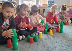 Dzieci układają wieże z kolorowych kubeczków według wzoru.