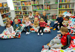 Dzieci siedzą na wielkich poduchach w czytelni- czekają na rozpoczęcie zajęć.
