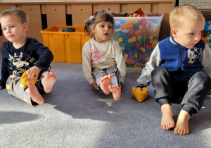 Dzieci unoszą nogi do góry przekładając woreczek z ręki do ręki.