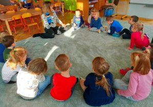 Dzieci siedzą w dużym kole na dywanie, słuchają uważnie Henia .