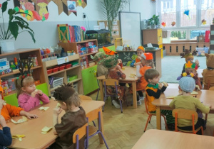 Dzieci siedzą przy stolikach i zjadają owocową przekąskę.