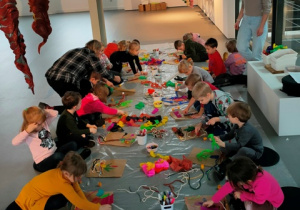 Dzieci siedząc na podłodze tworzą własne dzieła sztuki- Jesienne drzewa - wykorzystując w pracy różne materiały plastyczne.