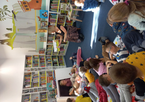 Dzieci siedzą na dywanie w czytelni i słuchają opowiadania.