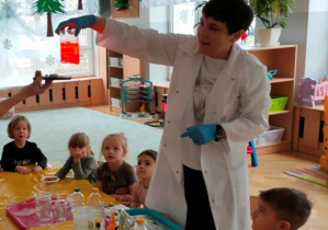 Chemik pokazuje dzieciom co się dzieje gdy wrzucimy tabletkę musującą do naczynia w którym znajduje się barwiona woda i olej.