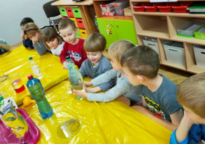 Dzieci próbują wykonać doświadczenie- poprzez ściskanie butelki skierować nurka na dno pojemnika.