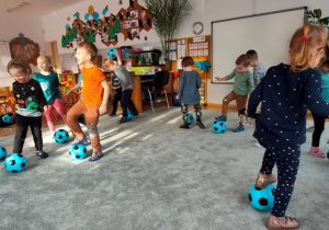 Dzieci turlają nogą piłkę w przód i w tył.