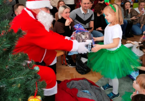 Mikołaj wręcza dziewczynce paczkę świąteczną.
