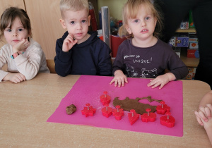 Dzieci po kolei wykrawają pierniczki w świątecznych kształtach.