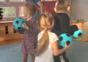 Dzieci oruszają się po dywanie z piłką w dłoniach.
