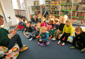 Dzieci siedzą na kolorowych poduchach w czytelni. Przygotowują się do spotkania z bajkowym bohaterem.