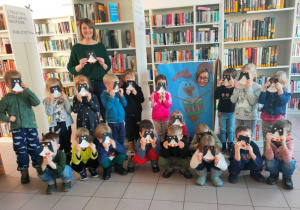 Dzieci ustawione w półkolach pozują do zdjęcia- ich twarze zasłonięte są sylwetami pingwinów.