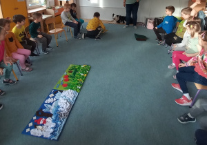 Dzieci siedzą na dywanie i obserwują zajęcia z dogoterapii.