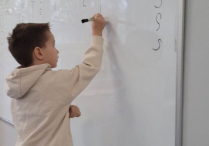 Chłopiec pisze na tablicy poznane litery.