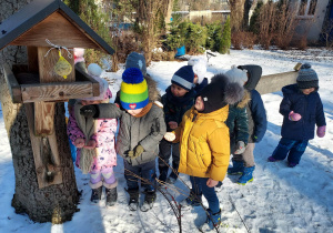 Dzieci po kolei wkładają do karmników ziarenka dla ptaków.