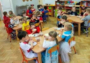 Dzieci przebrane w bajkowe stroje siedzą przy stolikach i jedzą śniadanie.