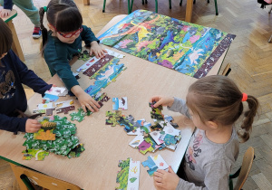 Dziewczynki układają puzzle przedstawiające świat dinozaurów.