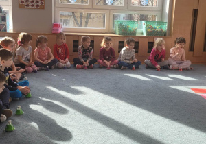 Dzieci siedzą na dywnanie i grają na dzwonkach.