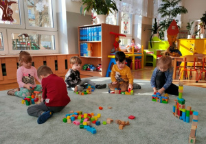 Dzieci na dywanie konstruują budowle z klocków.