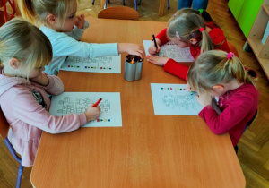 Dzieci siedząc przy stoliku wykonują zadanie graficzne.