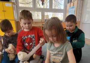 Dzieci na dywanie bandażują urazy swoich maskotek.