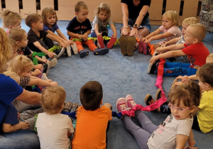 Dzieci siedzą na dywanie trzymając na nogach gumę sensoryczną.